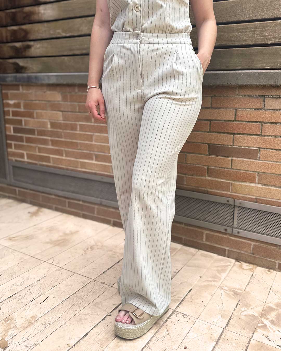 Chica lleva puesto un pantalón estilo pinza muy elegante en color beige a rayas.