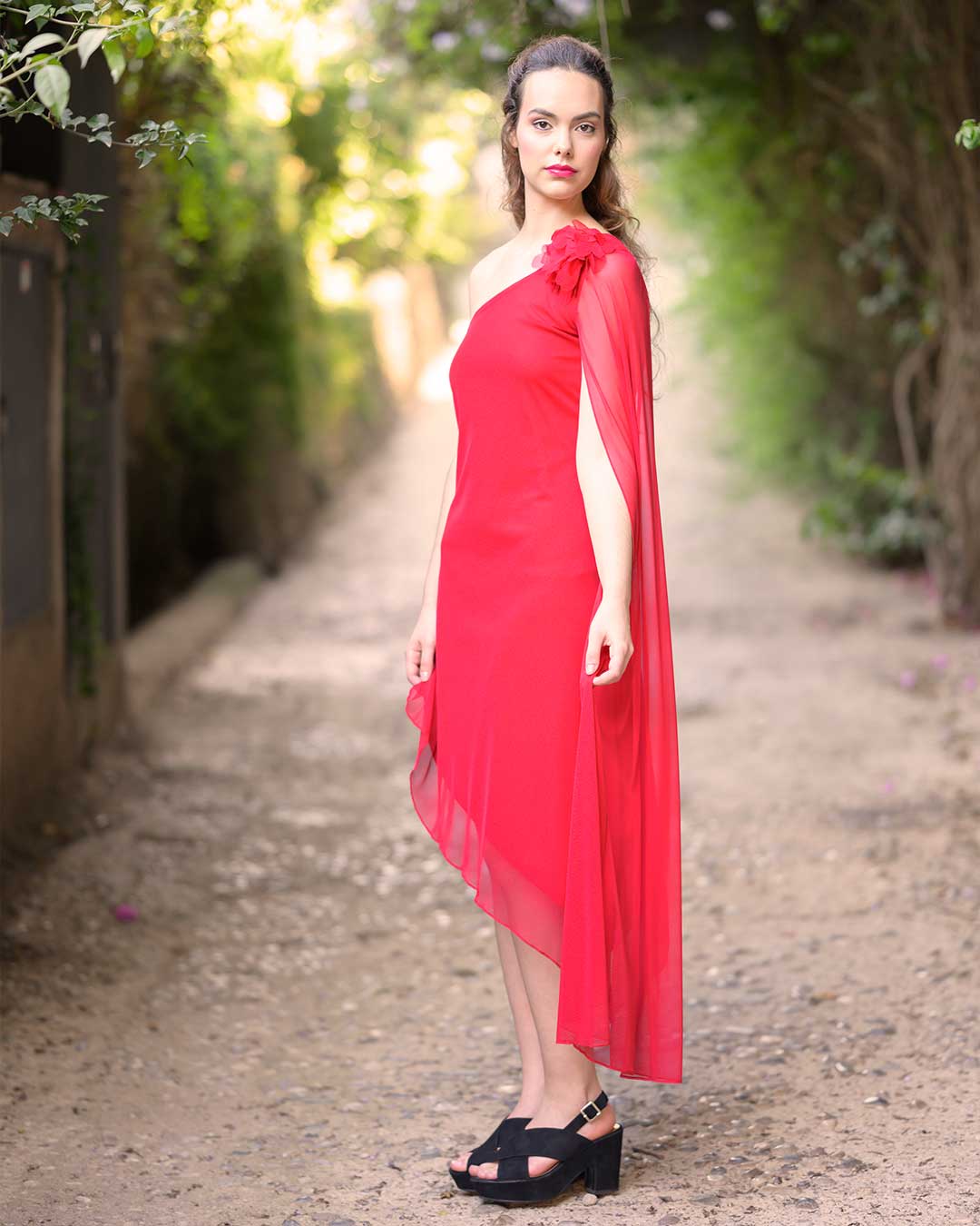 Vestido corto de fiesta de costado en el que se puede ver la manga larga de capa de gasa y el aplique floral del hombro en color rojo.