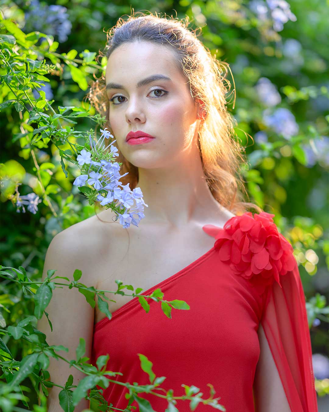 Vestido rojo de fiesta con mangas asimétricas y aplique floral de gasa en el hombro.